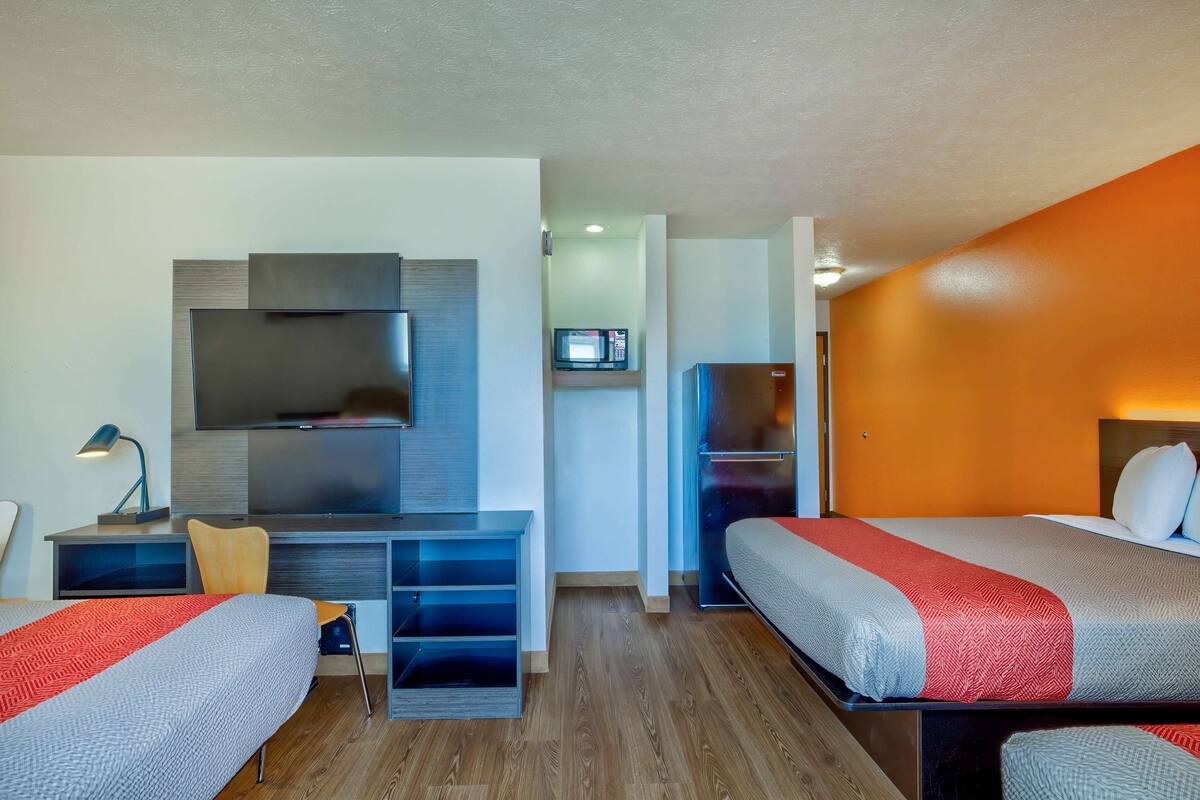 Ein modernes Hotelzimmer mit zwei Betten, einem Schreibtisch mit Stuhl, einem flachbildfernseher an der Wand, einer Mikrowelle und einem Kühlschrank.