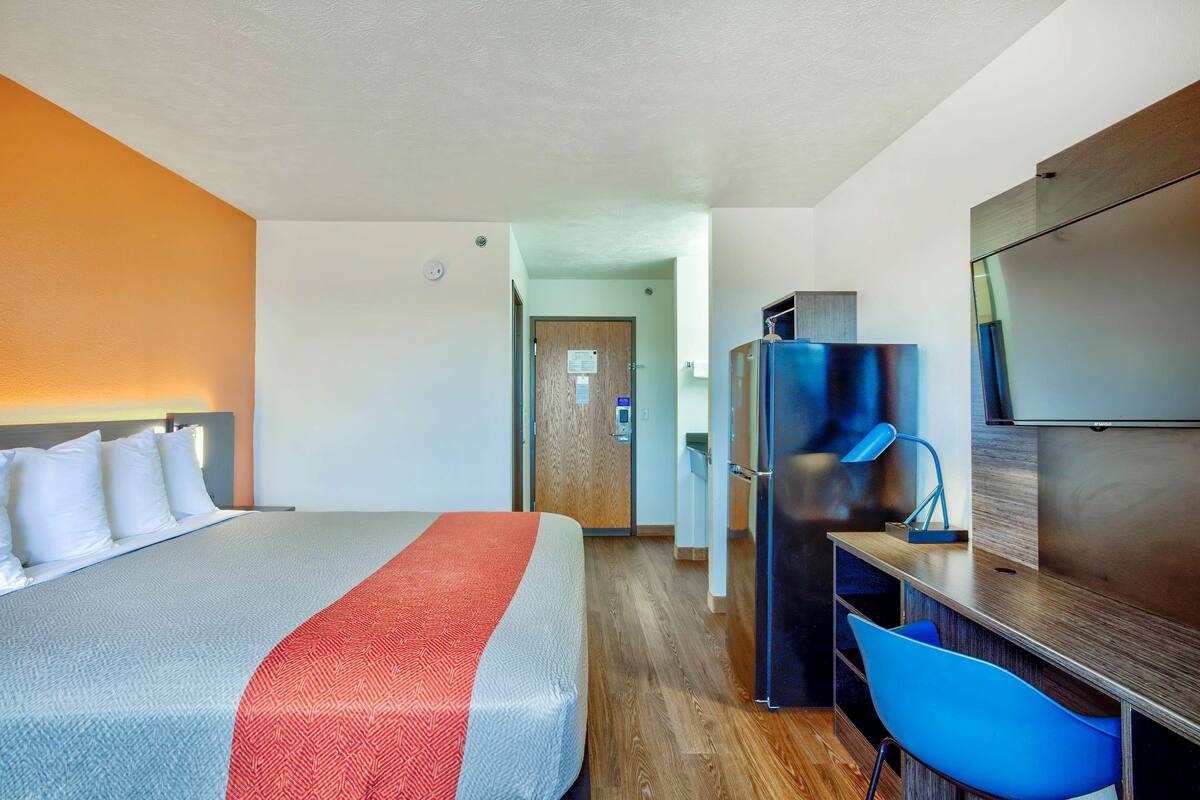 Ein Hotelzimmer mit einem Bett, einem Schreibtisch mit Stuhl, einem Kühlschrank und einem Fernseher.