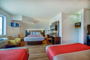 Ein Hotelzimmer mit einem großen Bett, zwei Einzelbetten, einem Schreibtisch, einem Sessel, einem Fernseher und einer Heizung.