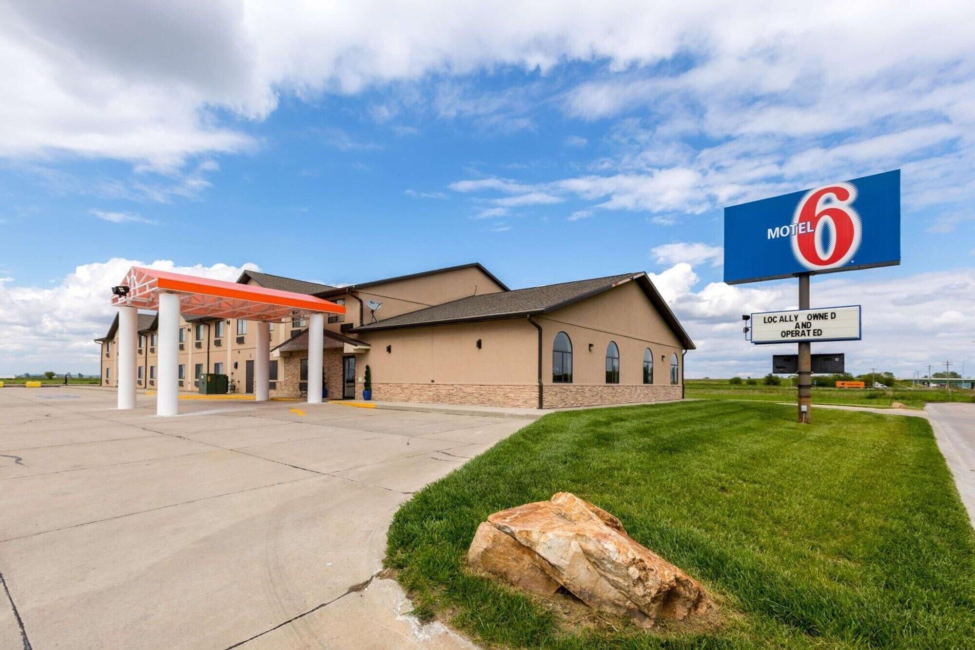 A motel with a large sign, a covered parking area, and a well-maintained lawn.