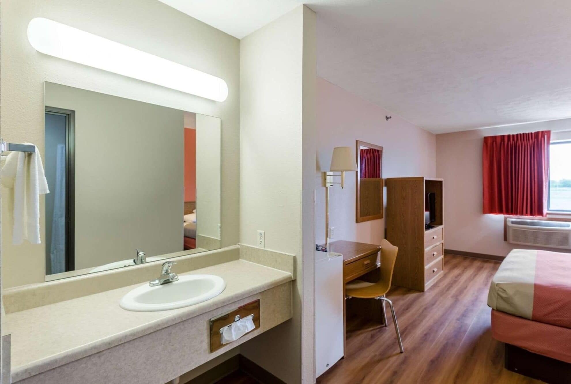 Habitación de hotel con un espejo grande, un lavabo, un escritorio, un armario y una cama.