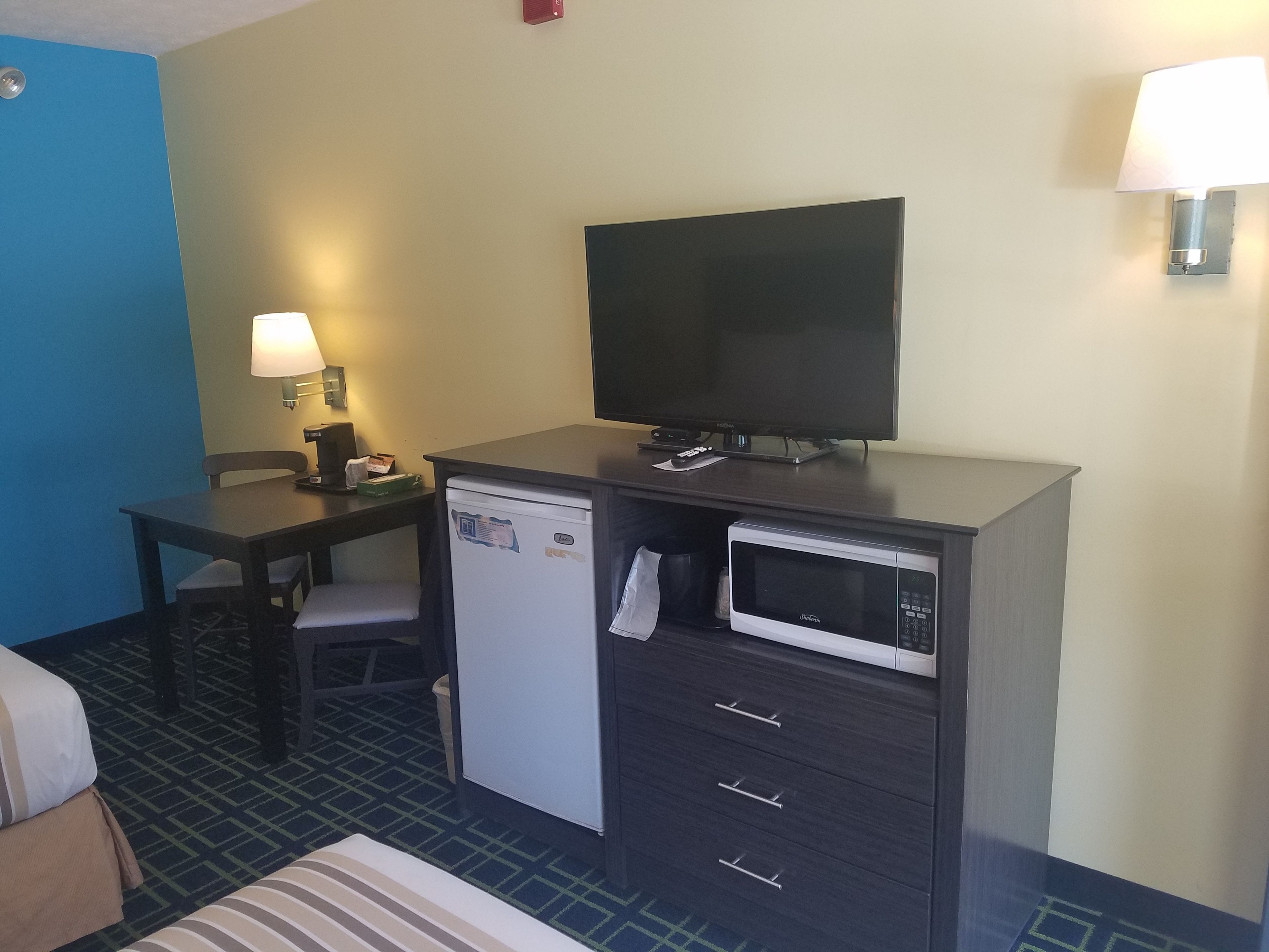 Een compacte hotelkamer met een bureau, een televisie, een magnetron, een koelkast en een stoel.