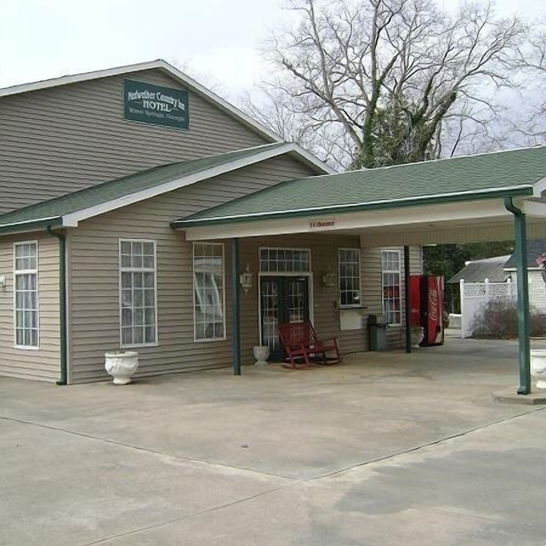 A two-story building with a sign reading "Pinehurst Country Inn." There is a covered porch with a rocking chair and a Coca-Cola cooler.