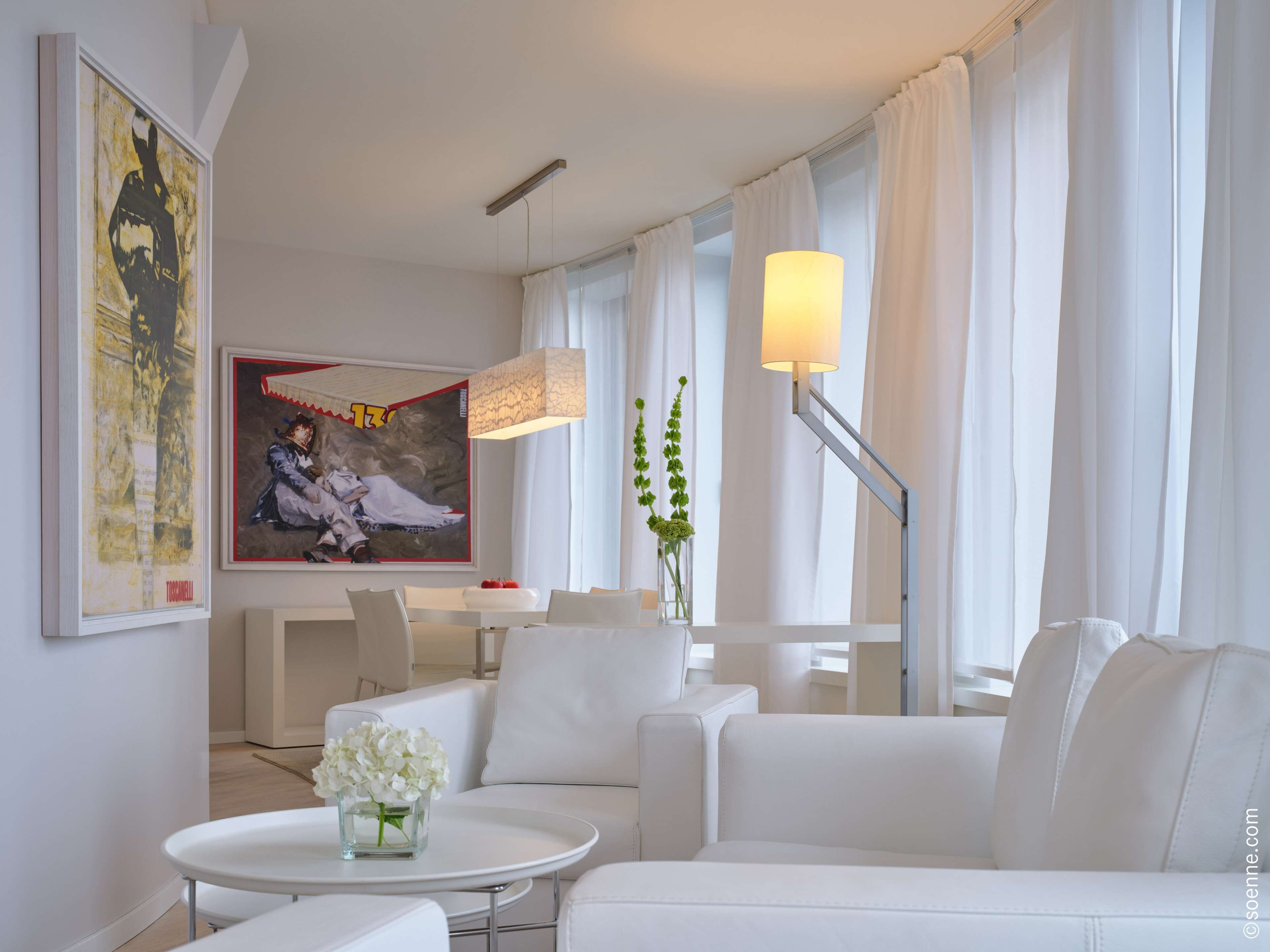 Un salon moderne avec des meubles blancs, un coin repas et un grand tableau accroché au mur.