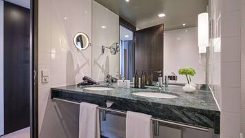 A modern bathroom with a large mirror, two sinks, a hairdryer, and a towel rack.