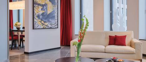 A modern hotel lobby with a beige sofa, two round tables, a large abstract painting, and a red curtain.
