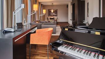 Ett hotellrum med ett piano, ett skrivbord med en telefon, en soffa och en tavla på väggen.