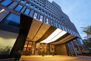 A modern hotel entrance with a glass facade, a covered entrance area, and potted plants.
