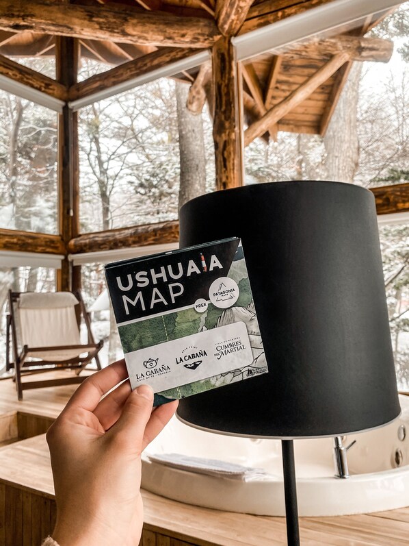 A hand holding a Ushuaia Map brochure with a wooden cabin interior in the background.