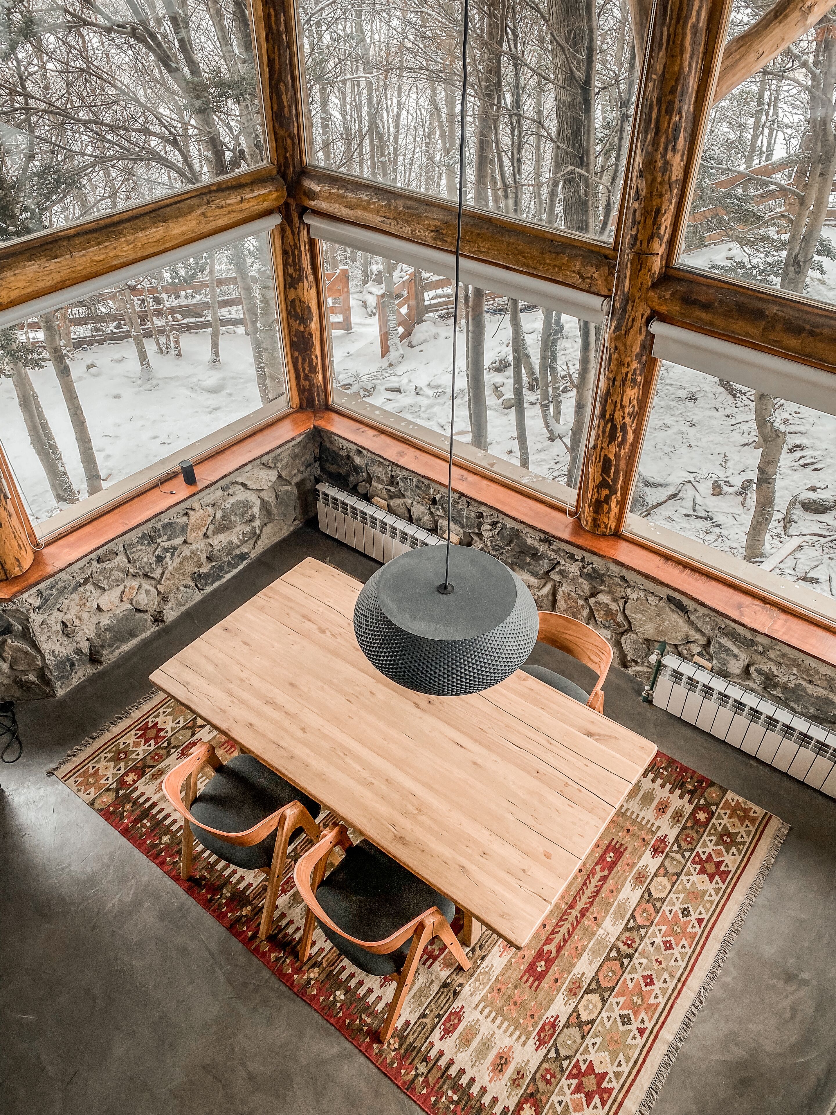 Un rincón acogedor con una mesa y sillas de madera, una alfombra estampada y una pared de piedra.