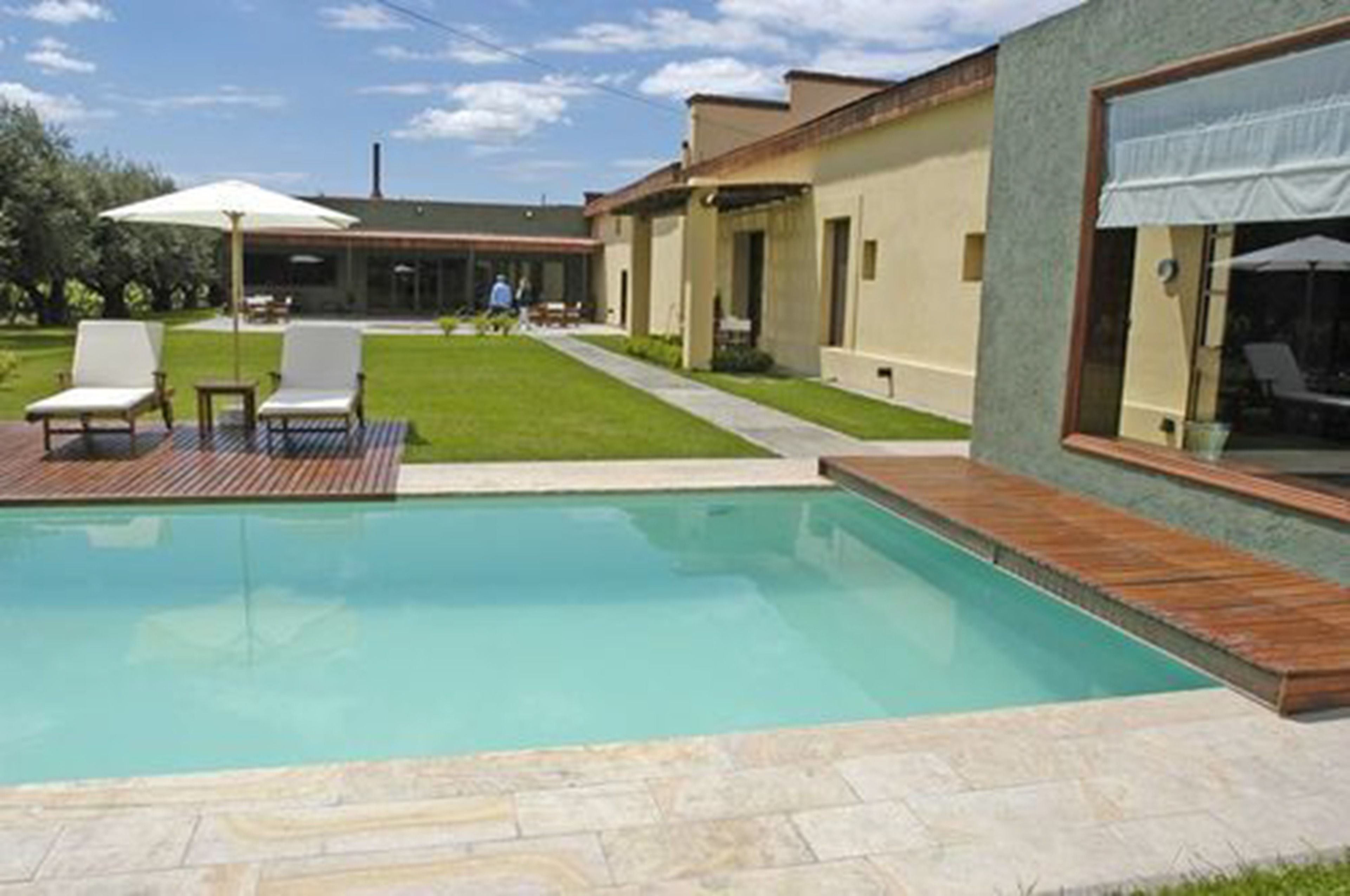 Un área de piscina moderna con una piscina azul cristalina, terraza de madera y dos sillas reclinables blancas.