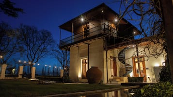 Una casa de dos pisos con un balcón, un jarrón grande y una escalera de caracol.