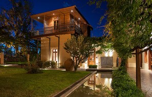 Una casa de madera de dos pisos con un balcón, un estanque y un jardín bien cuidado.