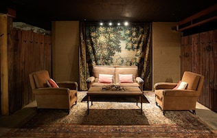 Una habitación acogedora con un sofá y dos sillones, un tapiz estampado y techo de madera.