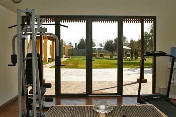 Un gimnasio en casa con cinta de correr, máquina de pesas y un amplio ventanal corredera que da a un jardín.