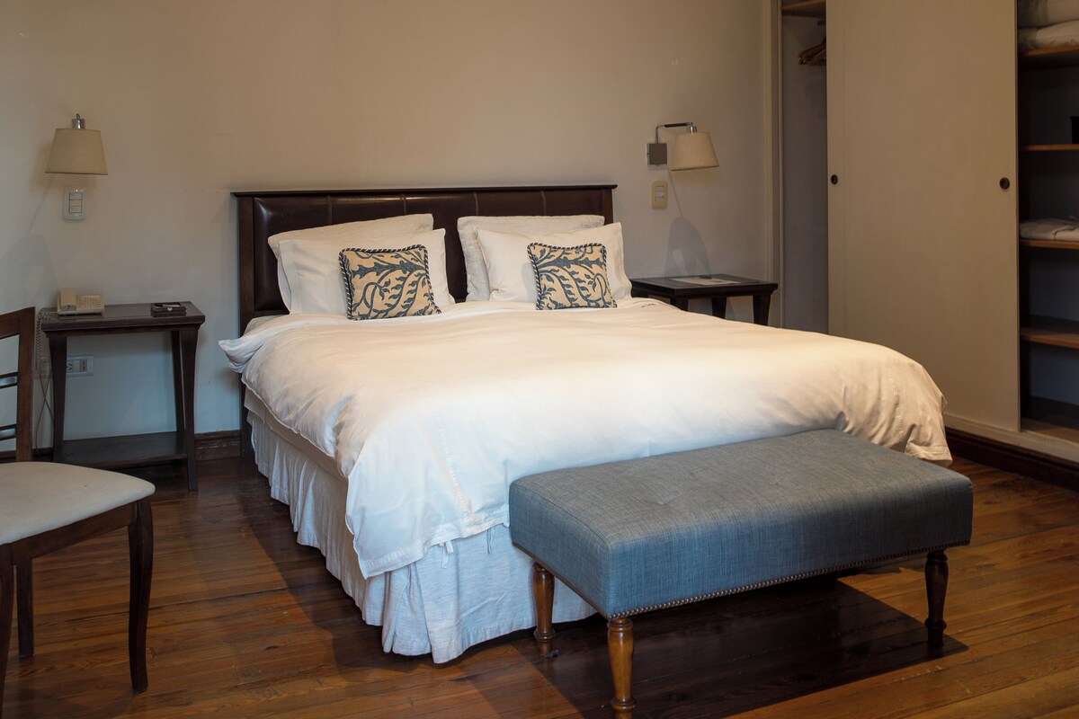 A neatly arranged bedroom with a large bed, bedside tables, a bench, and a walk-in closet.