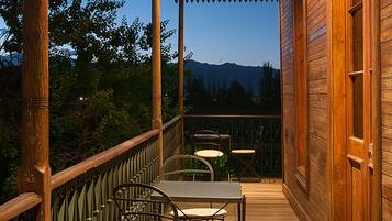 A wooden deck with a table and chairs, overlooking a mountainous landscape.
