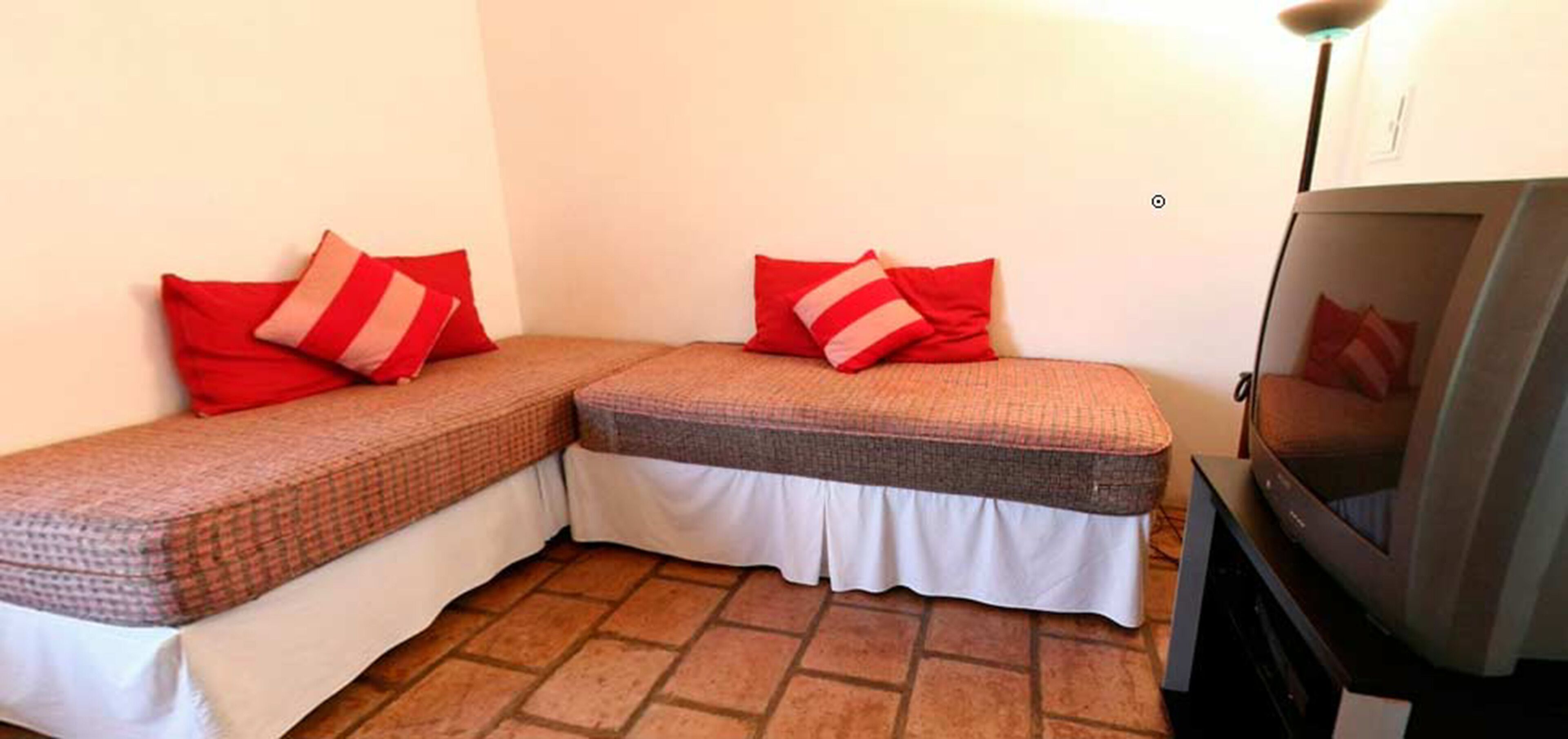 A small room with two single beds, each with red and white striped pillows, and a television on a stand.