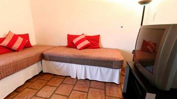 A small room with two single beds, each with red and white striped pillows, and a television on a stand.