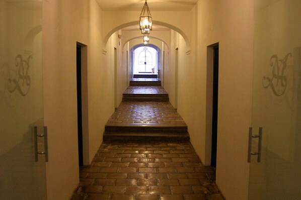 A hallway with a brick floor, white walls, and a chandelier. - El Manantial del Silencio (Purmamarca)