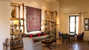A cozy living room with a sofa, a coffee table, and a dining area with chairs. There are shelves with decorative items and a large tapestry on the wall. - El Manantial del Silencio (Purmamarca)