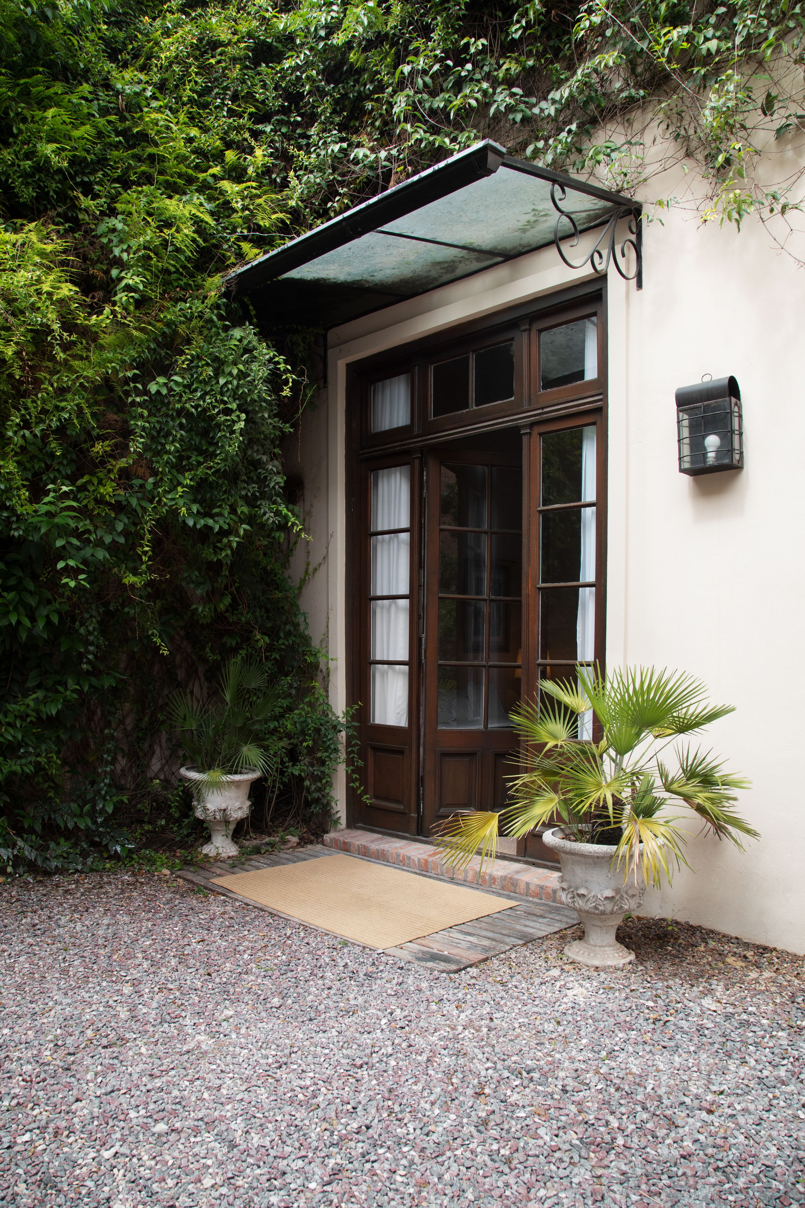 A building with a wooden door and windows, surrounded by greenery and a gravel path.