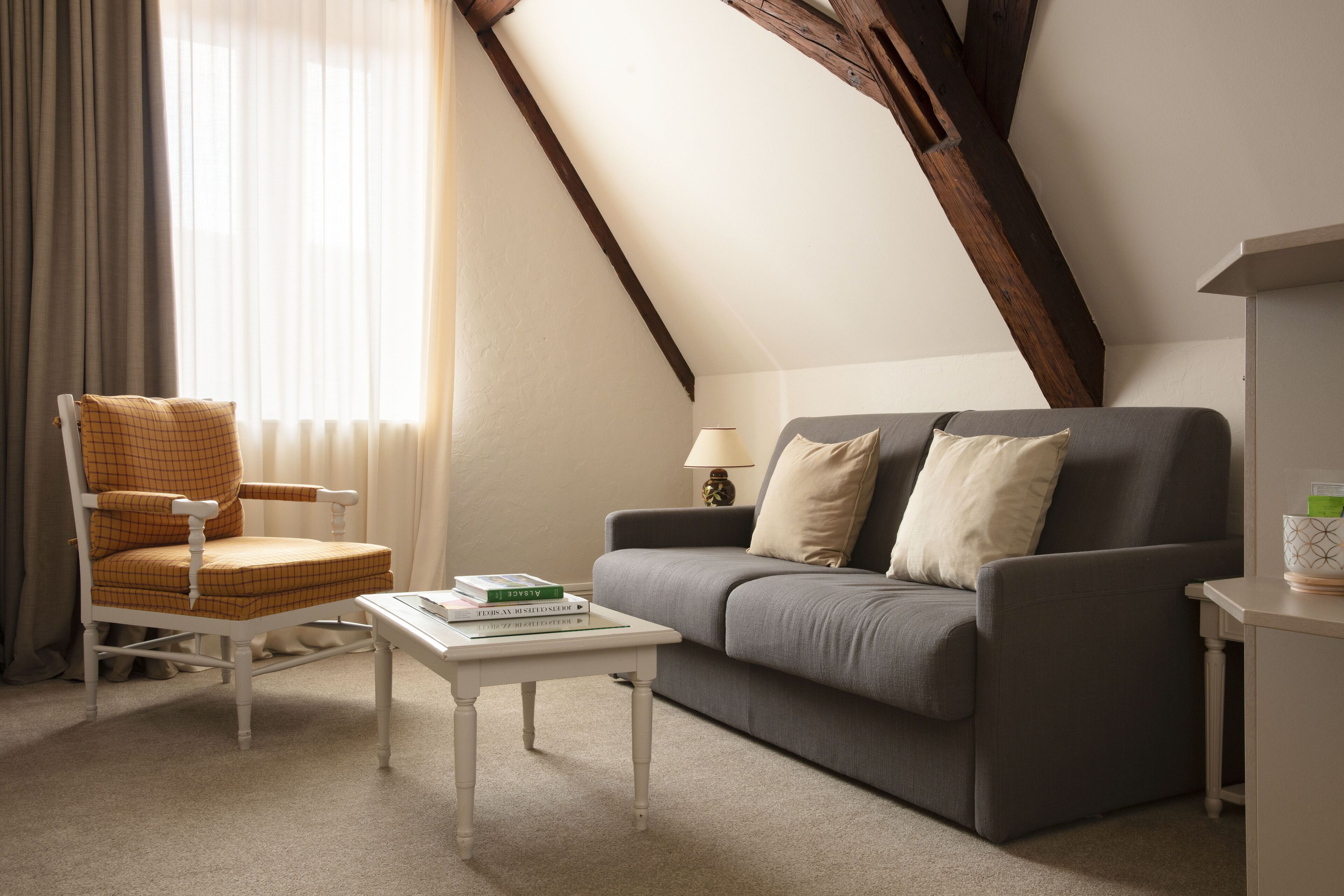 Una sala de estar acogedora con techo alto, un sofá gris, una silla de madera, una mesita blanca y una lámpara.