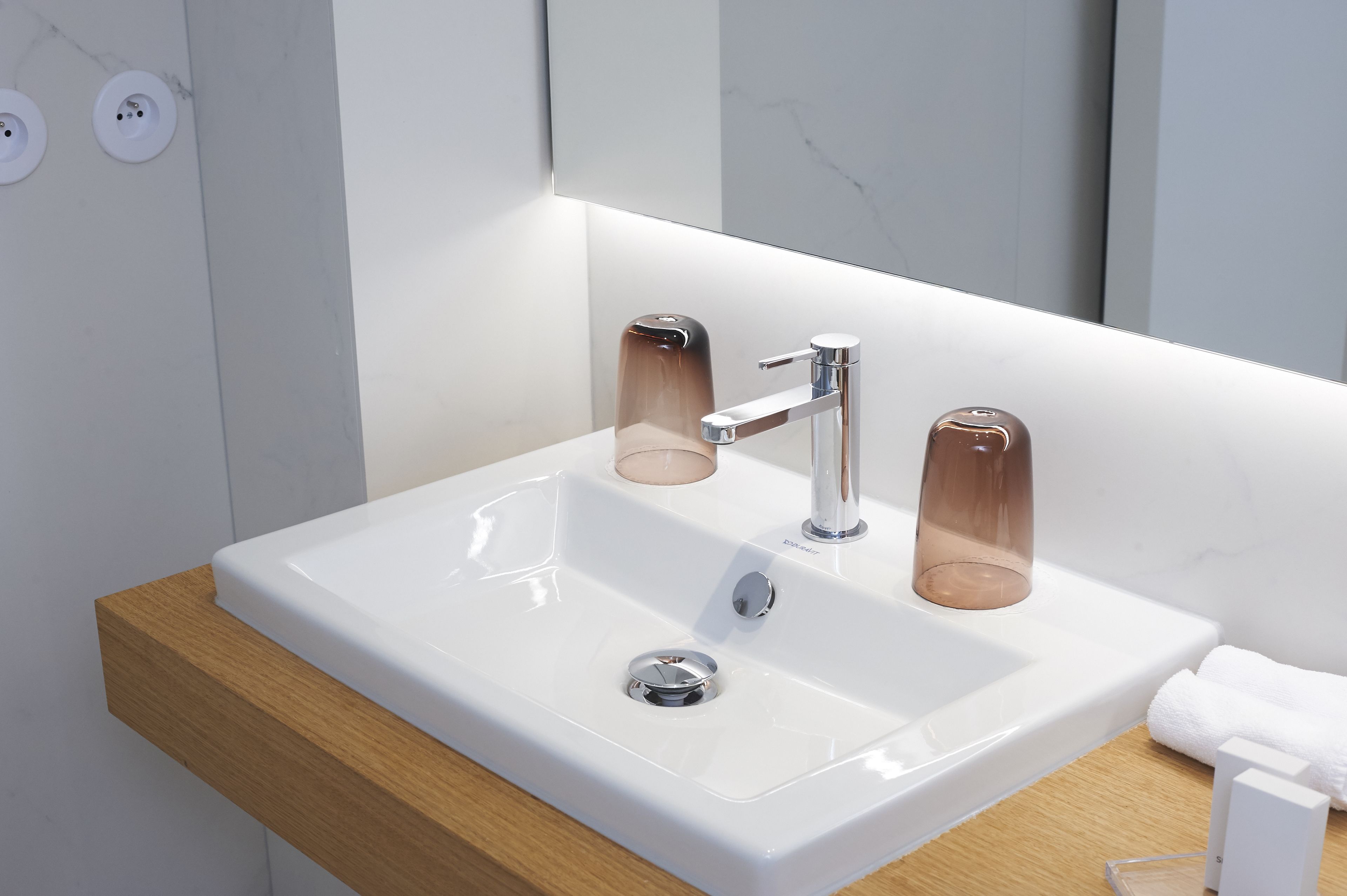 A modern bathroom with a white sink, chrome faucet, and a glass soap dispenser.