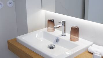 A modern bathroom with a white sink, chrome faucet, and a glass soap dispenser.
