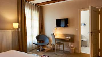 Ein Hotelzimmer mit einem Bett, einem Schreibtisch mit Stuhl, einem Fernseher und einem durchgegangene Tür erkennbaren Badezimmer.