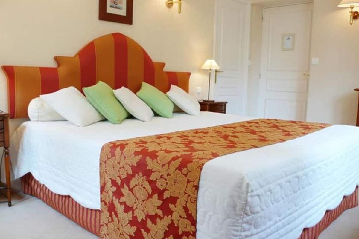 A hotel room with a large bed, a wooden nightstand, two wall-mounted lamps, and a door.