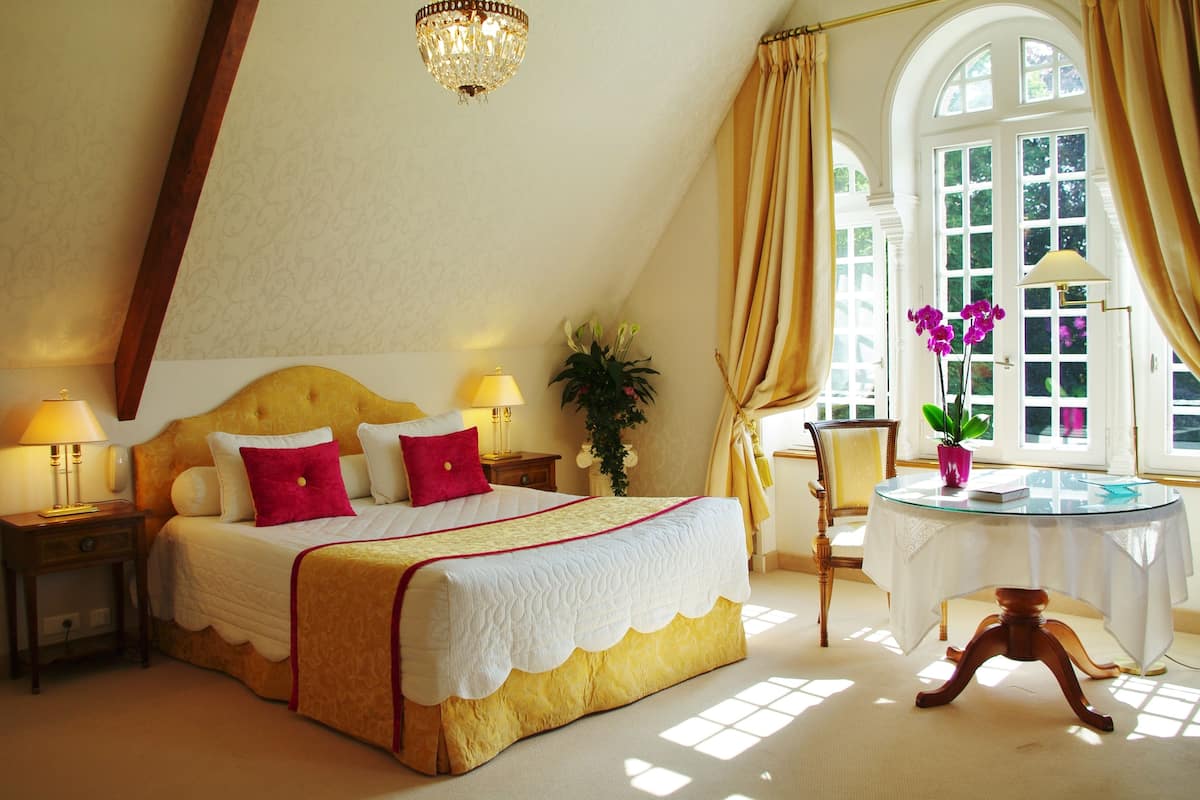 A bedroom with a large bed, a round glass table, and a window with curtains.