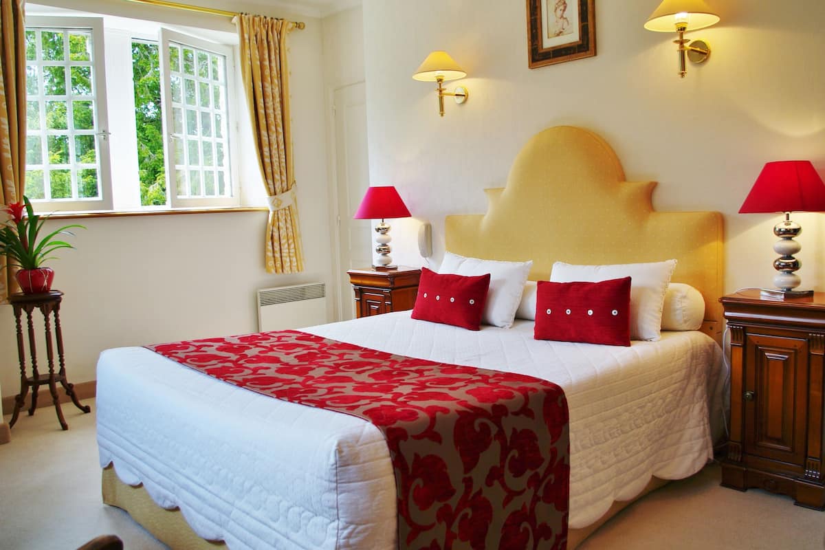 A neatly made bed with a red and white patterned bedspread, two bedside lamps, and a window with curtains.