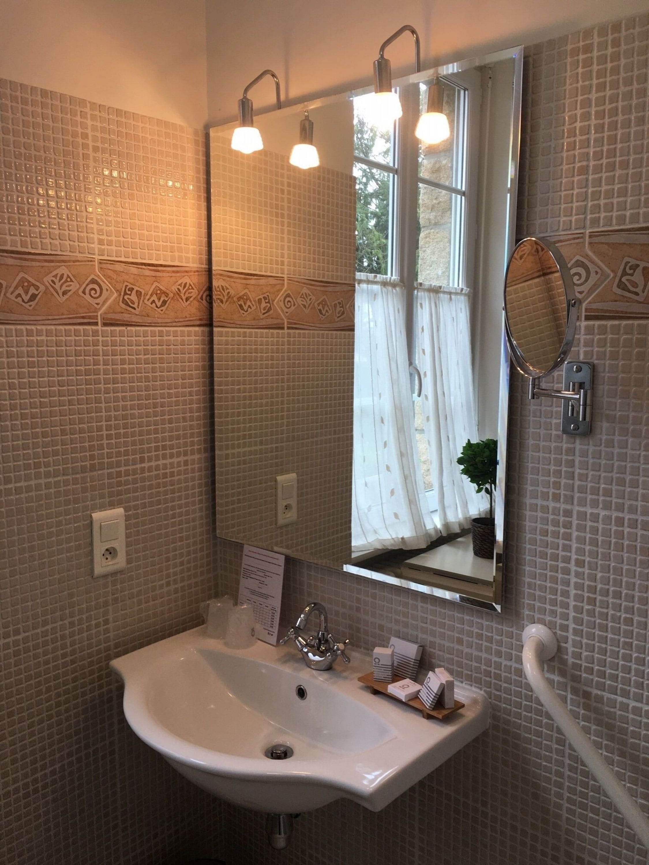 Une salle de bain avec un lavabo blanc, un miroir et une fenêtre avec des rideaux.