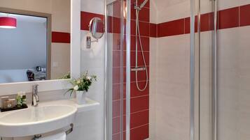 A modern bathroom with a glass-enclosed shower, a white sink with a mirror, and red-tiled walls.