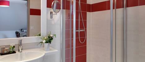 Un baño moderno con ducha envuelta en vidrio, un lavabo blanco con espejo y paredes de azulejos rojos.