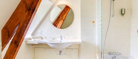 Un baño moderno con una viga de madera, un espejo redondo, un lavabo y una ducha.