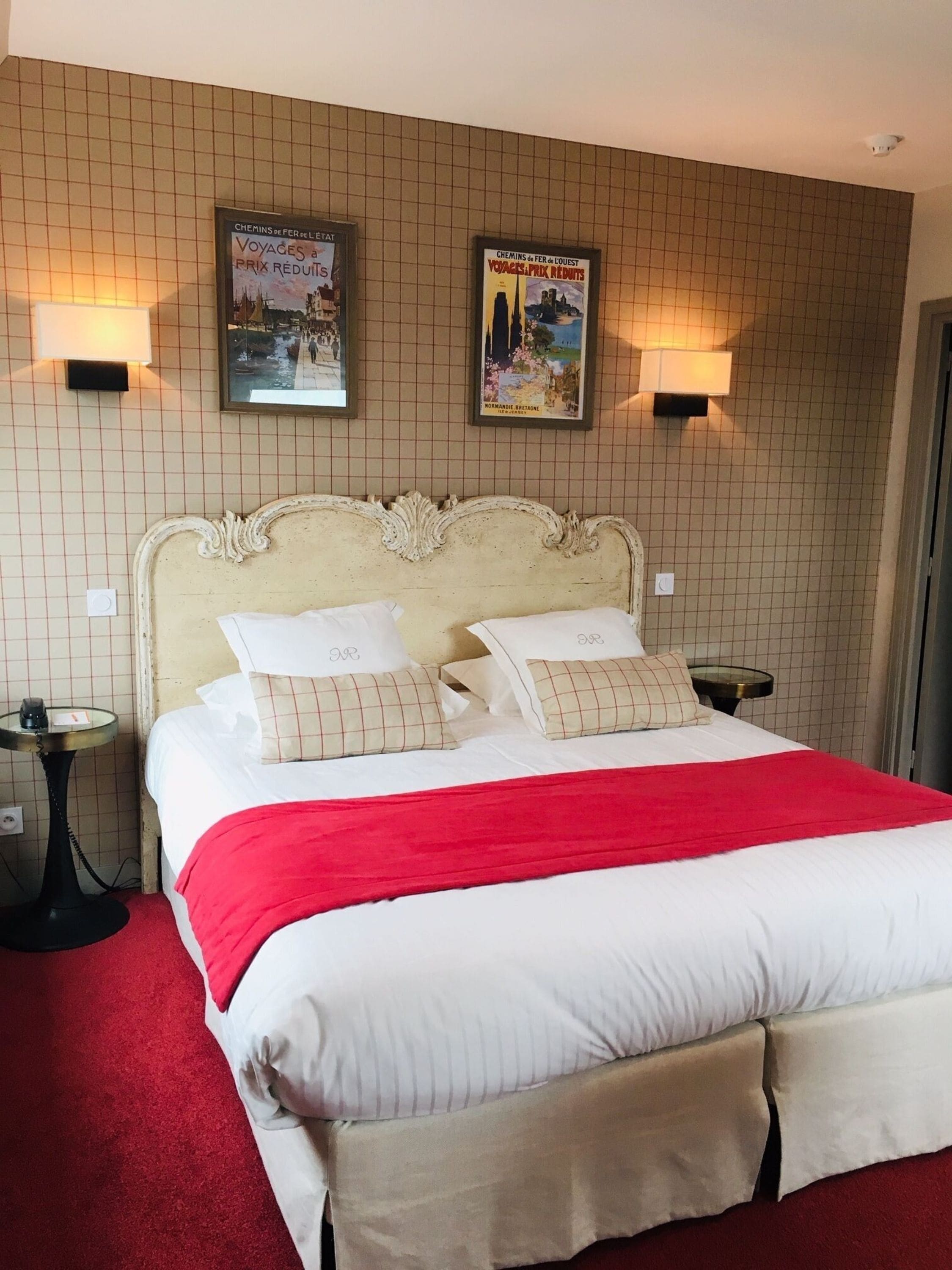 Een hotelkamer met een groot bed, twee wandlampen en twee posters aan de muur.
