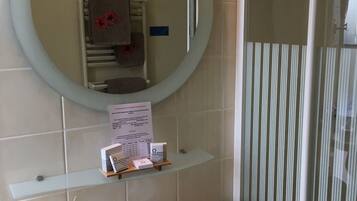A bathroom with a round mirror, a sink, and a towel rack. There is a sign on the wall and a glass shower enclosure.