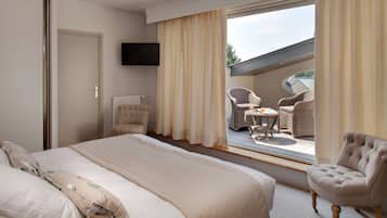 Een hotelkamer met een groot bed, een stoel, een tafeltje en uitzicht op een terras met rieten meubels.