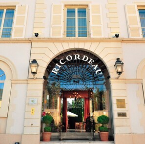 The entrance of Ricordeau hotel with a classical facade, arched windows, and a prominent entrance arch.