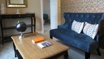 A living room with a dark blue sofa, a wooden coffee table with books and a globe, a black console table with a globe, a mirror with a green frame, and patterned wallpaper.