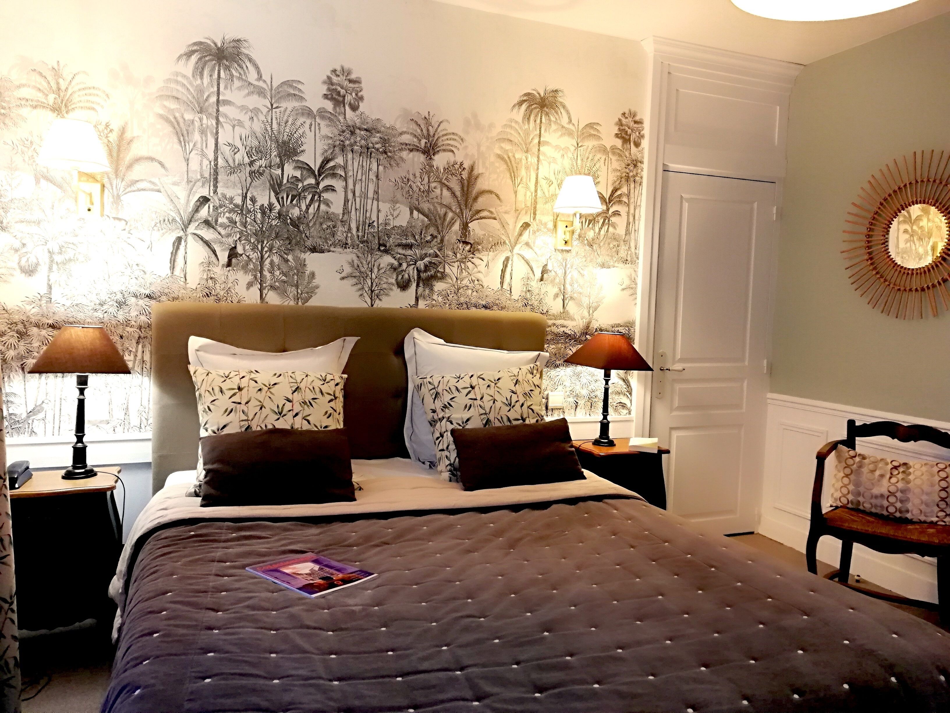 A bedroom with a large bed, two bedside lamps, a wall mural, and a door.