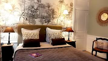 A bedroom with a large bed, two bedside lamps, a wall mural, and a door.