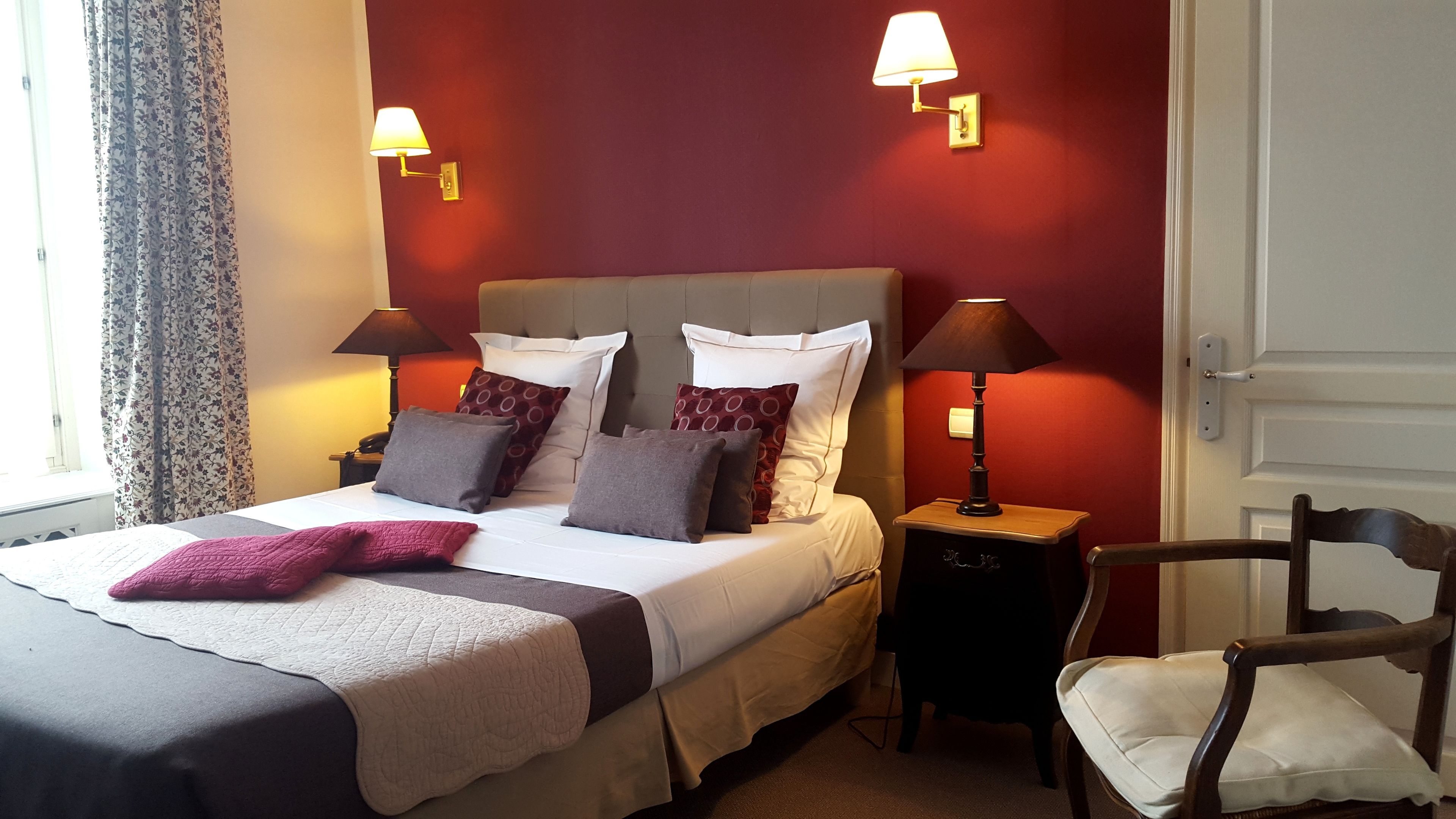 A neatly made bed with a pink throw, two bedside lamps, and a chair with a cushion.
