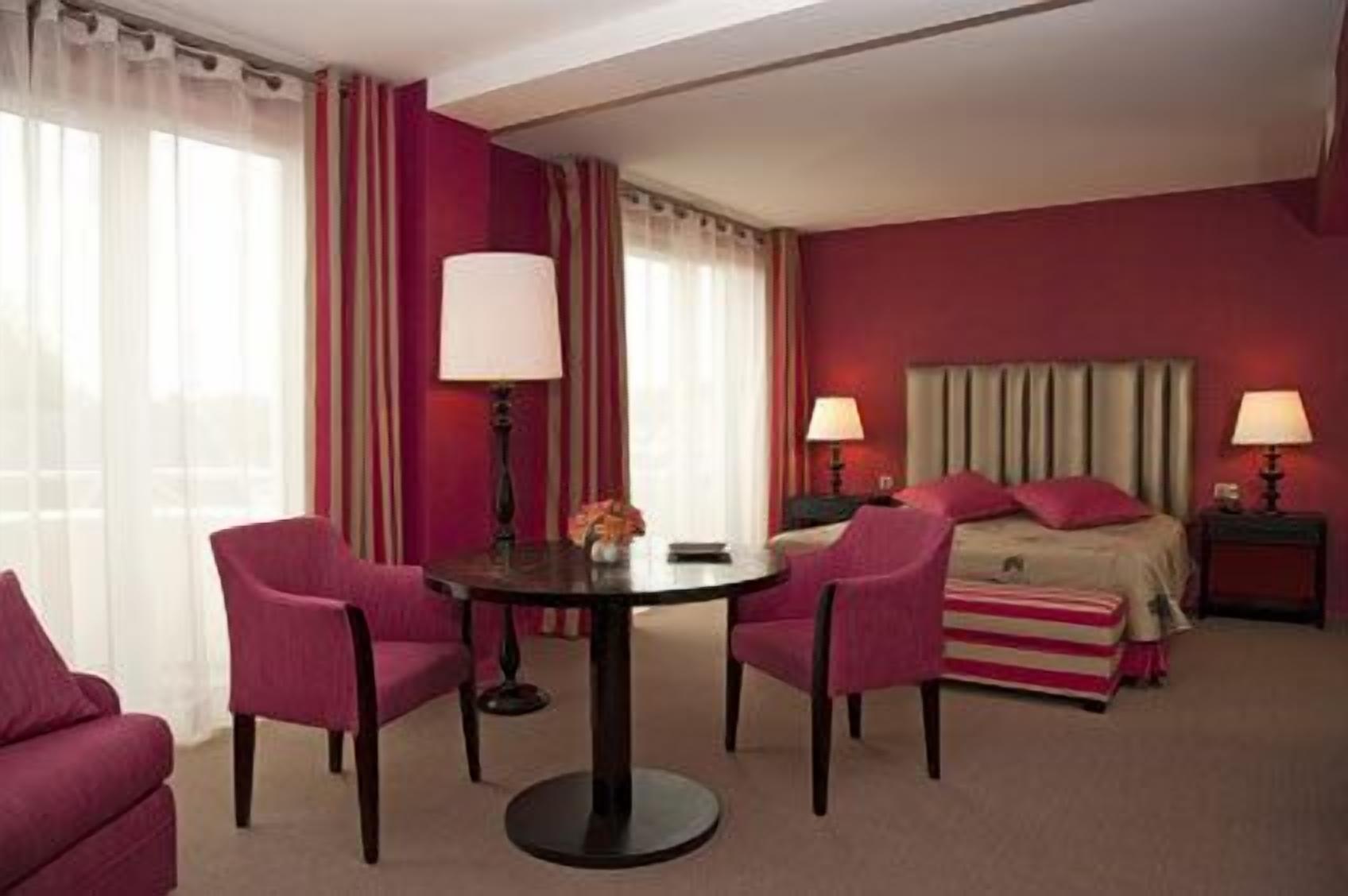 A hotel room with a bed, two chairs, a table, and two lamps.