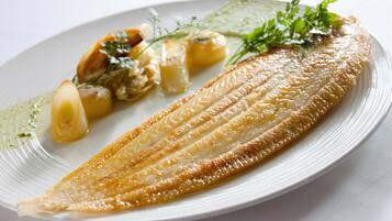 Un plato con un filete de pescado cocido, rodajas de limón y una guarnición de hierbas.