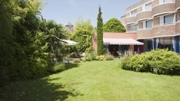 Um pátio com gramado, um edifício de tijolos e uma área coberta com telhado branco.