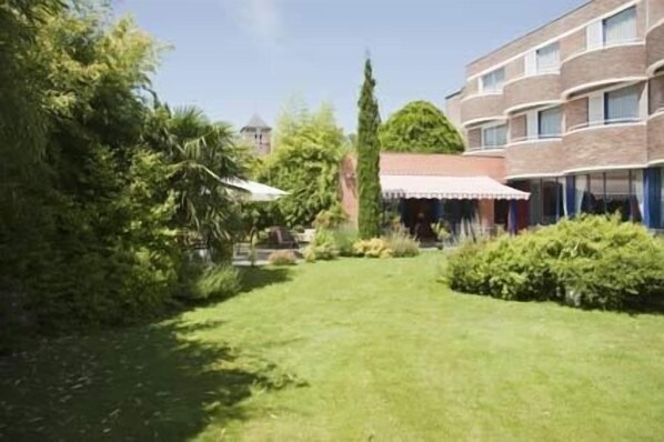 A courtyard with a lawn, a brick building, and a covered area with a white roof. - Grand Hôtel de Solesmes (Solesmes)