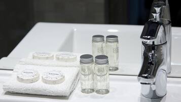 A bathroom with a white sink, a chrome faucet, and four bottles of Savon soap on the sink and a towel.
